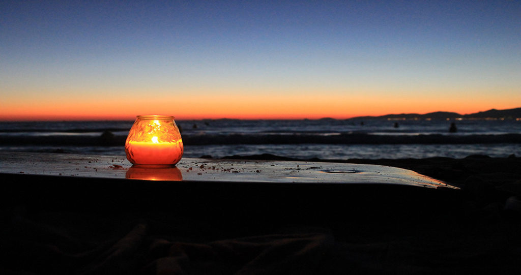 Coucher de soleil sur la plage, bougie allumée sur une table préparant la nuit.